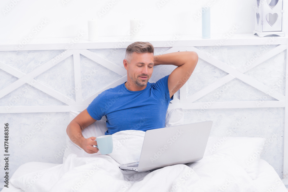 Relaxation in bed. Happy man drink coffee using laptop. Morning relaxation Relaxation in bed. Happy man drink coffee using laptop. Morning relaxation