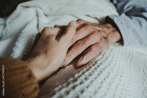 Close-up of a young woman's hand holding the hand of an old man lying on a bed