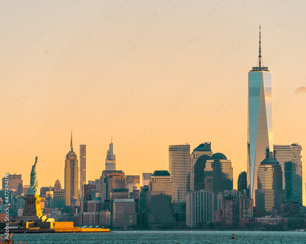 Obraz premium New York, NY - USA - Dec 26, 2021: Horizontal sunrise view of the Statue of Liberty in the New York Harbor, with the skyline of Manhattan, World Trade Center and Empire State building behind her.