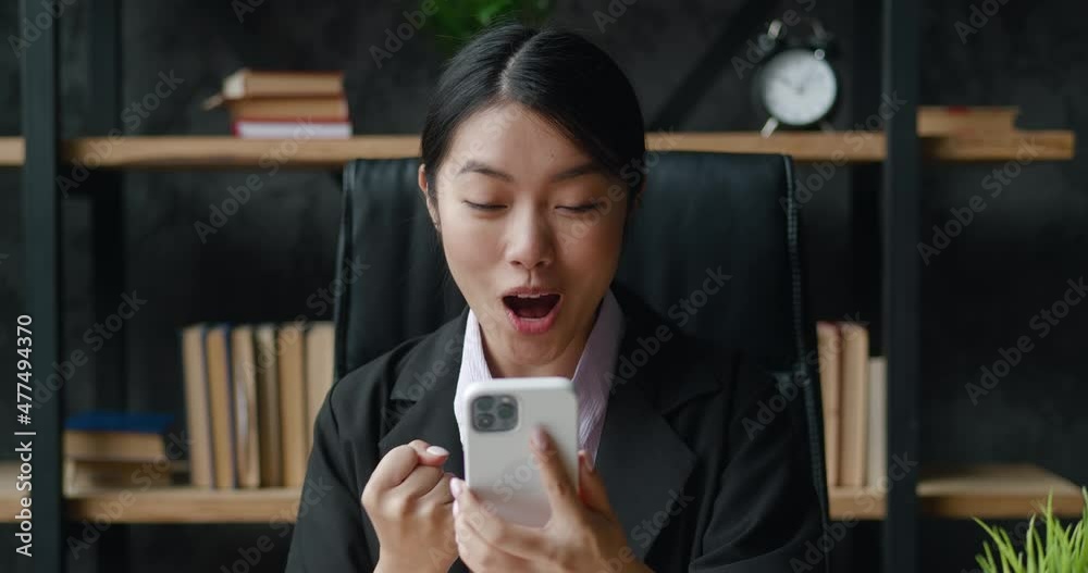Portrait of happy business woman enjoy success on smartphone sitting at modern office. Female celebrating victory with mobile phone indoors Portrait of happy business woman enjoy success on smartphone sitting at modern office. Female celebrating victory with mobile phone indoors