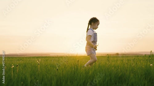 Active games for children in nature. Happy child, girl go on green grass in park, collects flowers on field, Kid smiles. Childhood dream. My daughter is having fun outdoors. Happy family, childhood