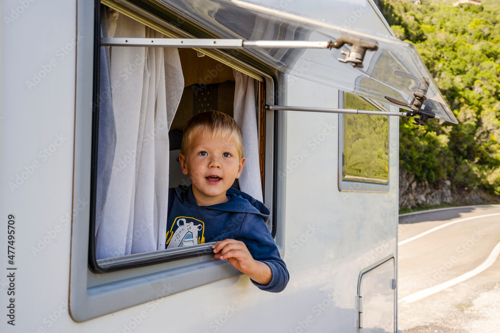 Happy small boy looking through the RV's window parked along the road