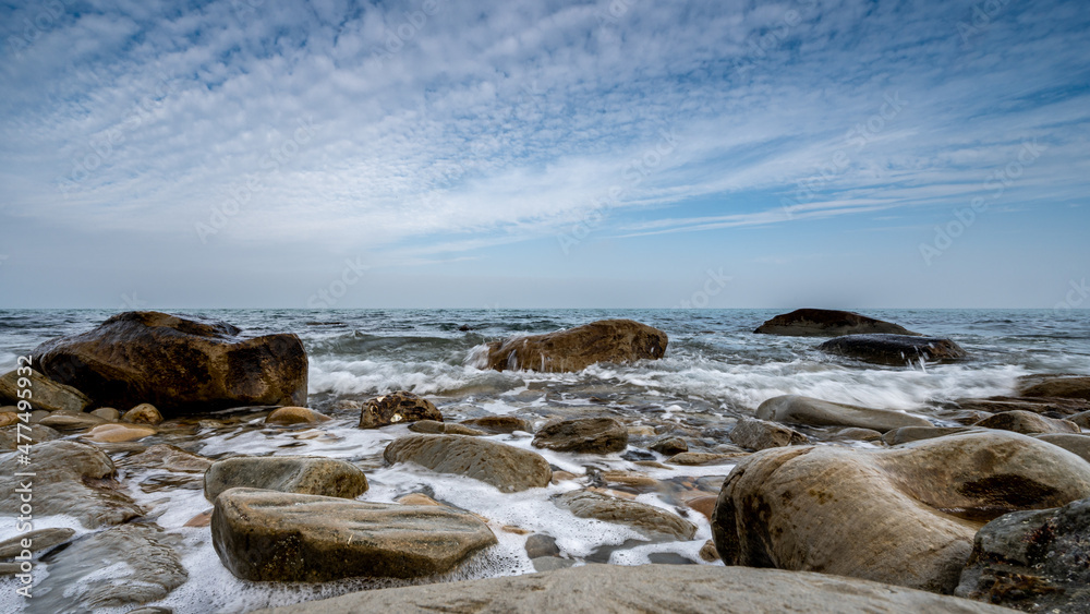 italy, december 2021: beach with pebbles, cliff, sea and cloudy sky