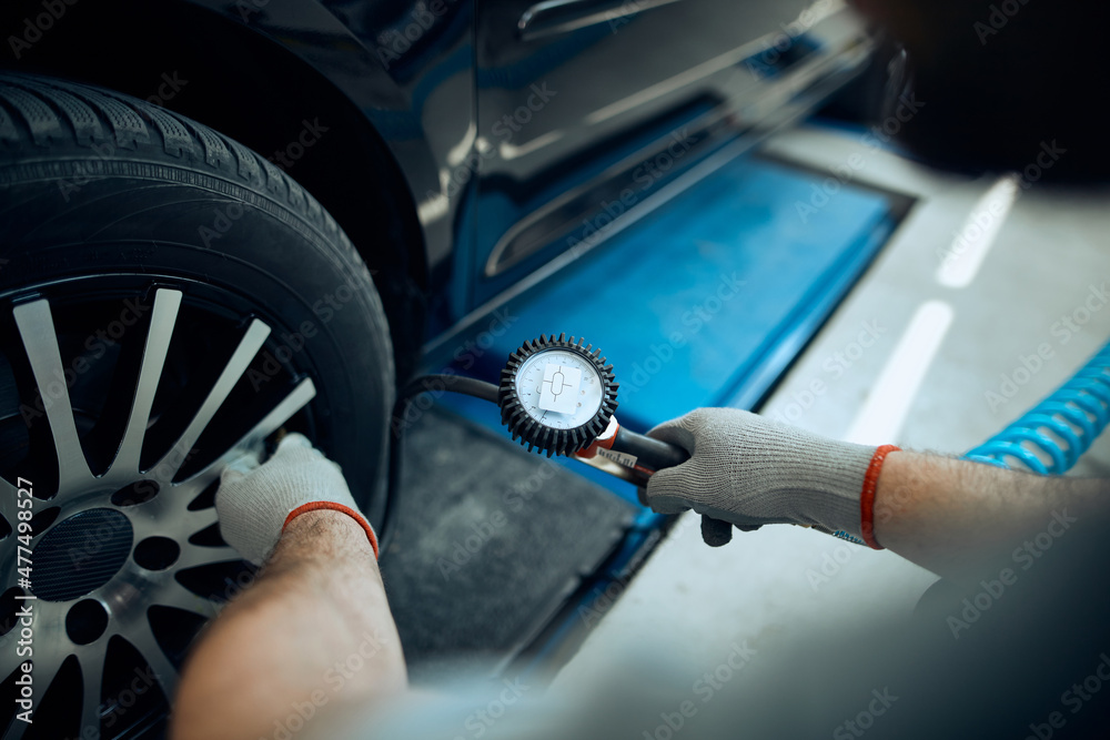 Close-up of mechanic checks pressure in car tire while working in service workshop.