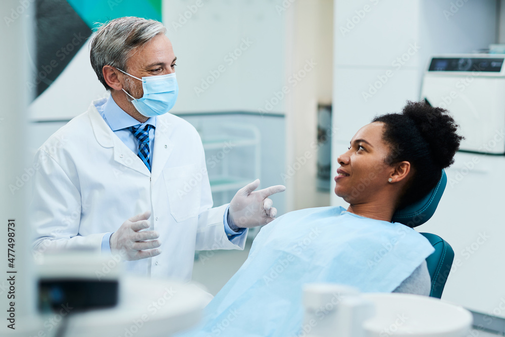 Obraz premium Dentist with face mask talks to black female patient during appointment at dentist's office.
