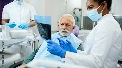 Senior man and his dentist analyse dental X-ray during appointment at dentist s office.