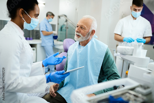 Happy senior man talks to his dentist during teeth check-up at dental clinic.