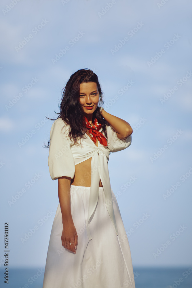 Slim adorable woman in summer beach clothes relaxing outdoors against sea background. A fashionable romantic young adult lady wearing a trendy white blouse, and skirt, standing at the beach Slim adorable woman in summer beach clothes relaxing outdoors against sea background. A fashionable romantic young adult lady wearing a trendy white blouse, and skirt, standing at the beach