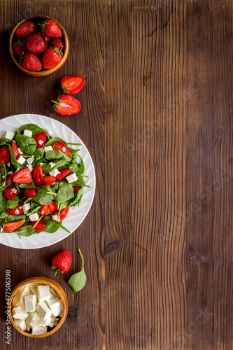White plate of green spinach salad with strawberry and goat cheese
