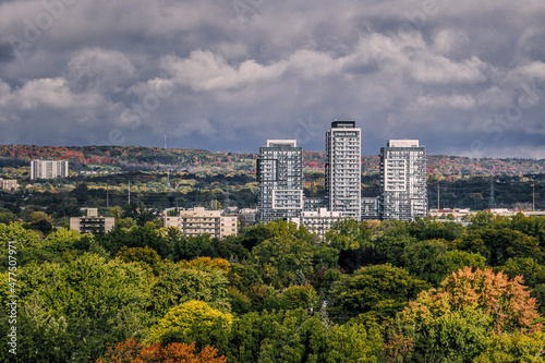 Clouds create shadows over a color changeing suburban forest with apartment buildings, a moody sky and mist on the heights
