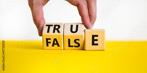 False or true symbol. Businessman turns wooden cubes and changes the word false to true or vice versa. Beautiful yellow table, white background, copy space. Business and false or true concept.