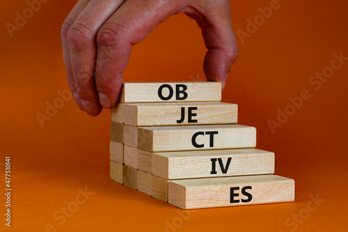 Objectives symbol. Wooden blocks stacking as step stair on beautiful orange background, copy space. The word 'objectives'. Businessman hand. Business and objectives concept.