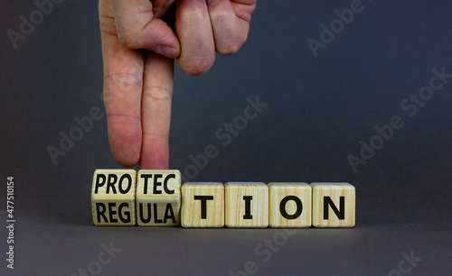 Protection and regulation symbol. Businessman turns cubes changes the word regulation to protection. Beautiful grey table, grey background, copy space. Business, protection and regulation concept.