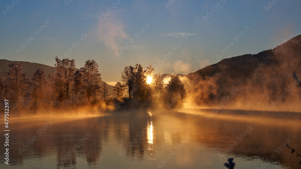 Fototapeta premium Sunrise over the river Hallingdalselva. Shot at Nesbyen, Norway. It is December and minus 20 degree outside. The water in the river is warmer than the air so therefor the smoke on the river. Frost. 