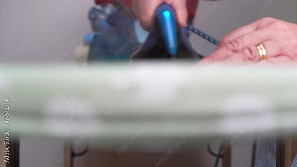 Woman hand irons striped shirt with a steam iron on an ironing board.Old woman ironing.slider shot. Сlose-up. Woman hand irons striped shirt with a steam iron on an ironing board.Old woman ironing.slider shot. Сlose-up.