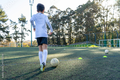 Child with his back to a soccer practice on a sunny day on an artificial turf field. Colored cones demarcating the practice to improve the use of the ball. Concept of sport for children. High quality photo