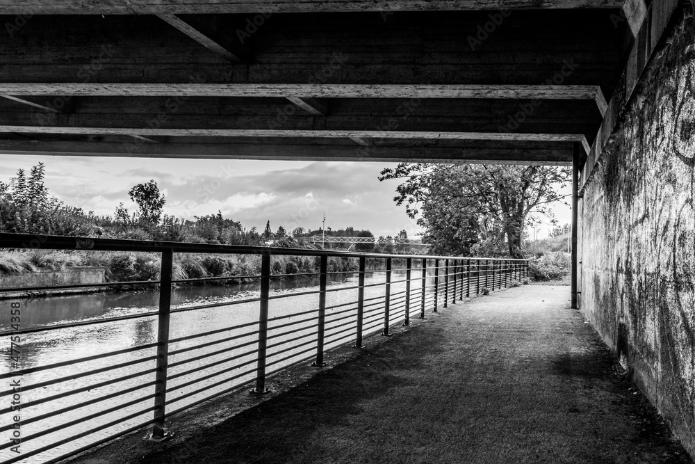 Intérieur d'un pont longeant une rivière, rempli de tags. (en noir et blanc)