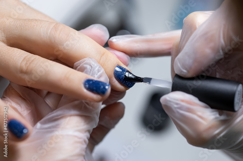 close-up, the master evens the color of the manicure with blue, applying gel polish on it with a brush