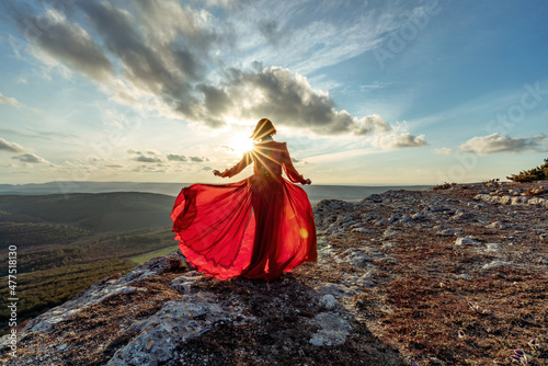 Rise of the mystic. sunset over the clouds with a girl in a long red dress. Stands on the mountain with a magical view.