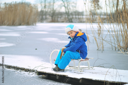 Child with a sled on a frozen lake. Dangerous fun on thin ice in winter.