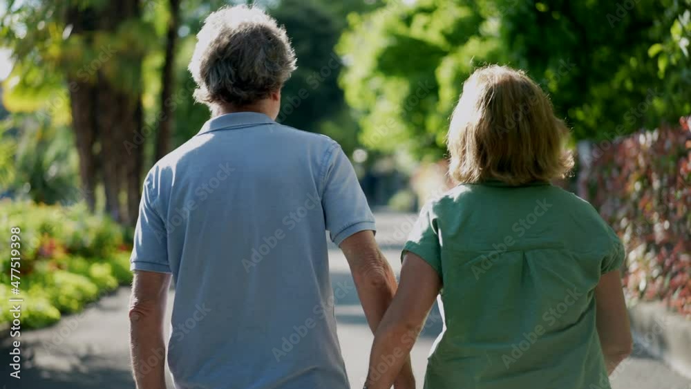 Romantic  senior husband putting arm around wife, back view of older couple walking together in green path