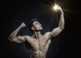 Young male athlete bodybuilder aestheticist posing against a dark background with sunlight in his hand. Healthy lifestyle and sports concept.