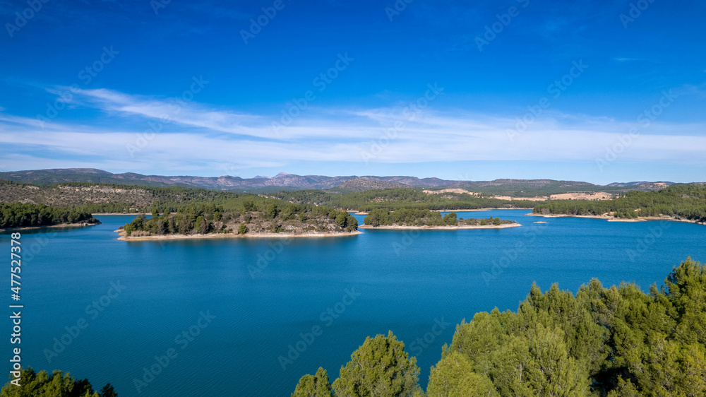 island with green trees sun over water reflection islet blue water vegetation shore aerial view drone photography horizon with mountains sunny blue sky