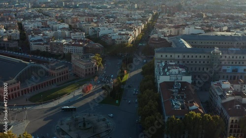 Descending footage of crossroads near Atocha train station. Tilt up reveal of buildings in urban district. Green trees lit by sun.