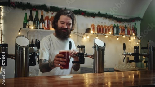 Bearded barman pouring lambic into glass close-up, foamy cherry beer. Bartender putting cider, alcohol fruit red drink on table. Fresh beverage on bar counter background in pub.  photo