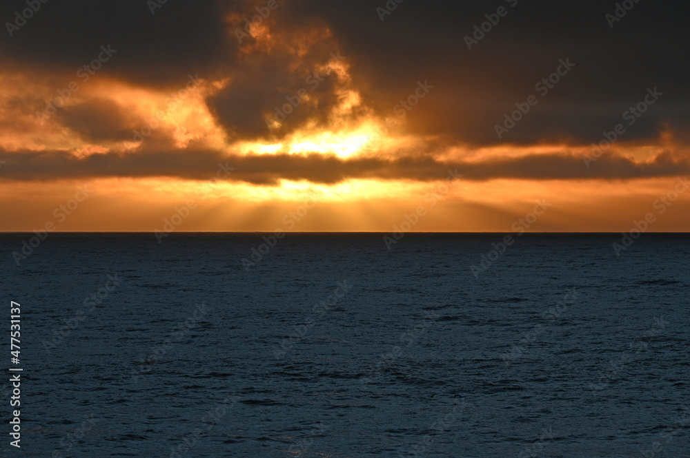 Sunset sun rays on flat Pacific Ocean.