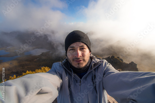 Hiker man selfie with winter clothes and a landscape of the valley with lakes and rocky mountains from top of Cerro Chirripo in Chirripo National Park in Costa Rica