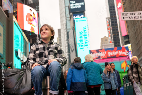 boy in jeans and plaid jacket sitting on post in new york city, time square