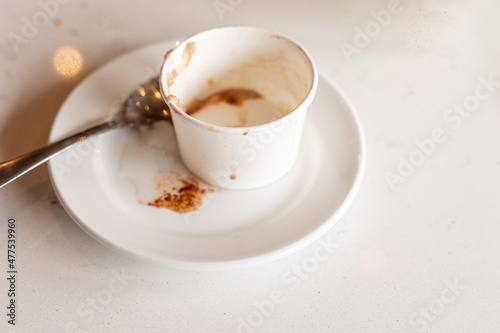 empty chocolate italian ices cup on white saucer with white table and spoom