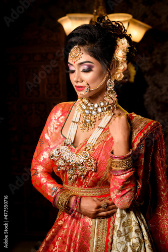 Portrait of very beautiful young Indian bride in luxurious bridal costume with makeup and heavy jewellery in studio lighting indoor. 