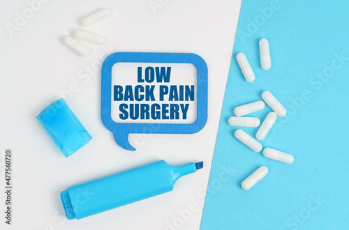 On a white and blue table are pills, a marker and a blue plaque with the inscription - Low Back Pain Surgery