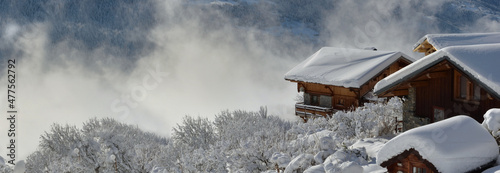 wooden chalets  in alpine village covered with snow overlooking cloudy valley landscape