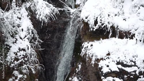 Slow motion shot of the water of the Jana waterfall flowing during the snowfall in winter at Kullu in Himachal Pradesh, India. View of the waterfall during the snowfall. Winter background.	 photo