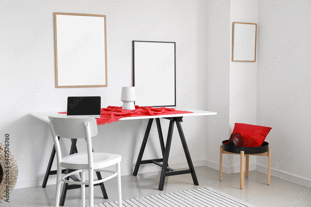 Modern workplace near light wall with blank posters Modern workplace near light wall with blank posters
