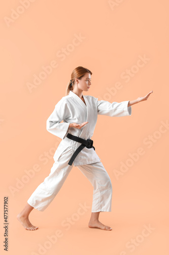 Young woman practicing karate on color background