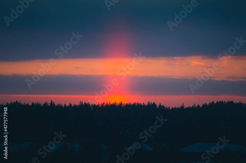 Bright orange vertical light pillar in winter  Lithuania. Optical phenomenon with sunlight ice crystals in the air. Selective focus on the details  blurred background.