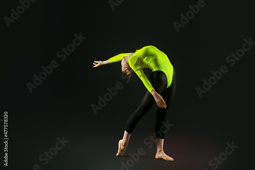 Beautiful young woman doing gymnastics on black background