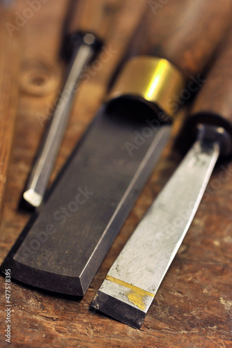 A vertical close up macro shot of three different sized metal chisels with wooden handles lying on a wooden workbench, Johannesburg, South Africa