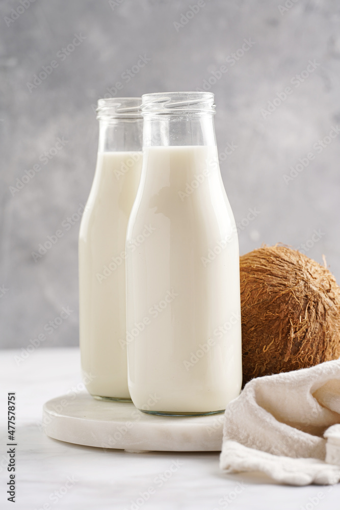 Two bottles with non-dairy milk and coconut on round marble board Two bottles with non-dairy milk and coconut on round marble board
