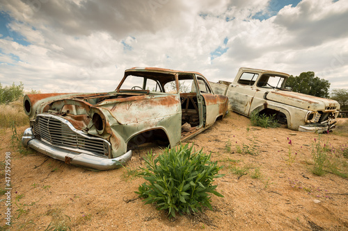 A horizontal shot of two abandoned vintage car wrecks on a stormy cloudy afternoon taken in Solitaire, which is a small settlement in the Khomas Region of central Namibia photo