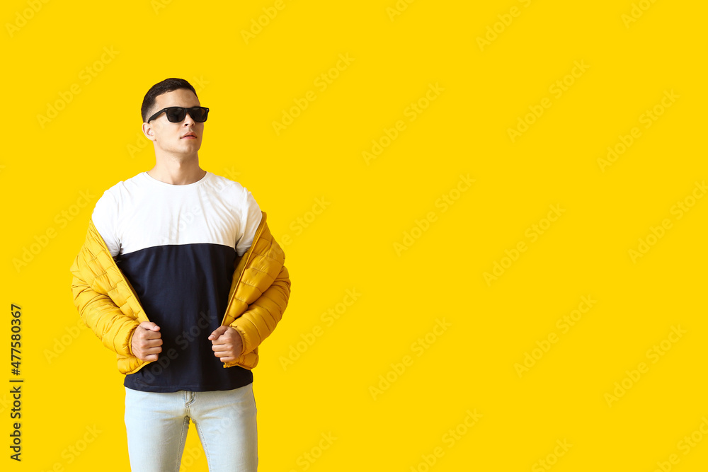 Young man in stylish sunglasses and jacket on yellow background Young man in stylish sunglasses and jacket on yellow background