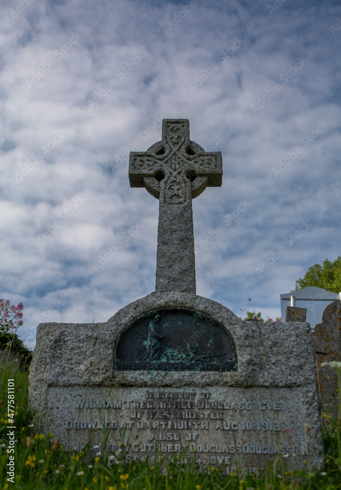 gravestone in the grass with celtic cross and cloudy sky in the background gravestone in the grass with celtic cross and cloudy sky in the background