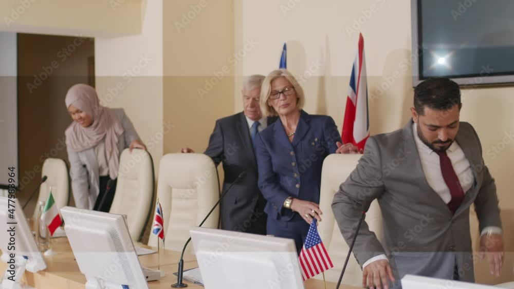 Medium shot of diverse male and female political leaders of different countries arriving at press conference, greeting audience in tabletop microphones