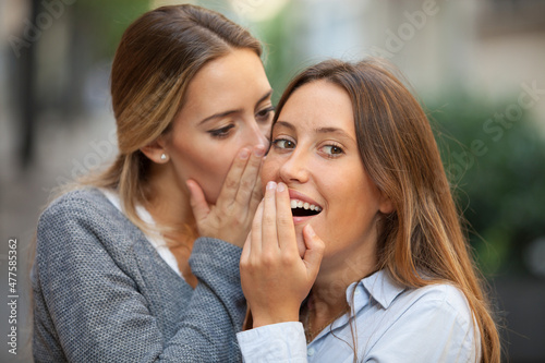 Beautiful woman whispers to her mate shocking news outdoors