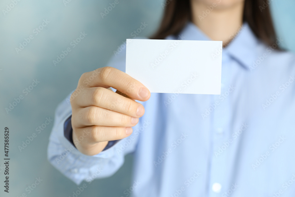 Woman holding blank business card on light blue background, closeup. Mockup for design