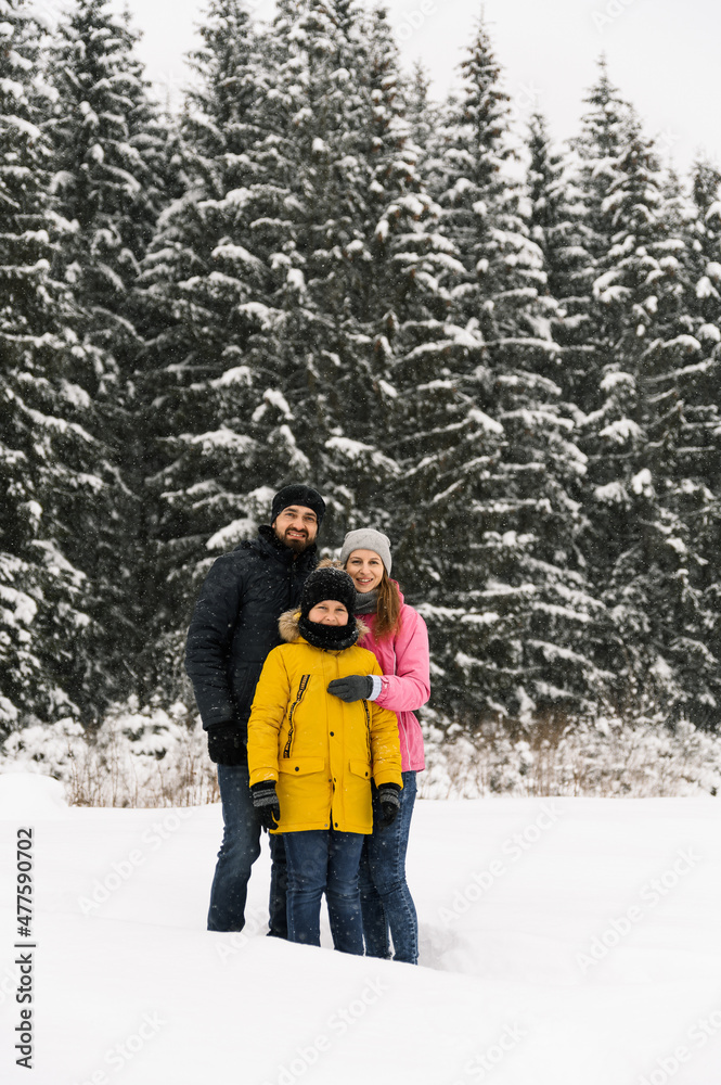 Happy family have fun in winter forest and looking at camera. Mother, father and son playing with snow. Family Christmas concept. Enjoying spending time together
